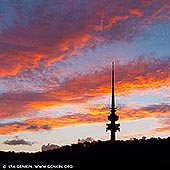 australia stock photography | Sunset over Black Mountain and Telstra Tower, Canberra, ACT, Australia, Image ID AU-ACT-CANBERRA-0019. As the sun dipped below the horizon, Black Mountain and the iconic Telstra Tower were silhouetted against a sky ablaze with fiery reds, oranges, and golds. The vibrant hues painted the clouds, creating a mesmerising backdrop for Canberra's skyline. Black Mountain, known as Galambary to the Ngunnawal people, rises 812 meters above sea level and is a significant natural landmark in Canberra. It forms part of the Canberra Nature Park and is home to diverse native flora and fauna. The mountain holds cultural importance for the Ngunnawal people, serving as a traditional site for ceremonies and gatherings. Perched atop this mountain is the Telstra Tower, a 195-meter-high telecommunications and observation tower completed in 1980. Originally known as Telecom Tower, it has become a prominent feature of Canberra's landscape, offering panoramic views of the city and surrounding regions. The tower is currently undergoing renovations, with plans to reopen in 2026, incorporating elements that celebrate Ngunnawal culture. This vivid sunset over Black Mountain and Telstra Tower captures the harmonious blend of natural beauty and cultural heritage that defines Canberra.
