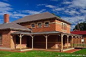 australia stock photography | Wentworth Court House, Wentworth, New South Wales (NSW), Australia, Image ID AU-WENTWORTH-0003. The Wentworth Court House building comprises a two storey structure with hip roof, complimented at the rear with identical single storey extensions displaying the same roof line. A straight pitched verandah surrounds the building, supported by chamfered posts adorned with elegant timber brackets. The upper level features three round headed windows highlighted by stucco hood trim. The ground floor windows are adorned in the same manner. The first entrance door consists of double circular panels and topped with a large fan light. The courthouse is bounded by a picket fence which traditionally adorned most properties in Darling Street, north of Sandwych Street. The structure is the dominant administrative building in the shire and a vital component of the streetscape complimenting surrounding heritage items including the Post Office and St Johns Church.