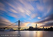 australia stock photography | Anzac Bridge at Sunrise, Glebe, Sydney, NSW, Australia, Image ID AU-SYDNEY-ANZAC-BRIDGE-0012. The Anzac Bridge is a large cable-stayed bridge spanning Johnstons Bay between Pyrmont and Glebe Island near the central business district of Sydney, Australia. The bridge forms part of the Western Distributor leading from the Sydney CBD and Cross City Tunnel to the suburbs of the Inner West and Northern Sydney. The photo made at sunrise on a partly cloudy day when the Sun highlighted clouds in golden hues.