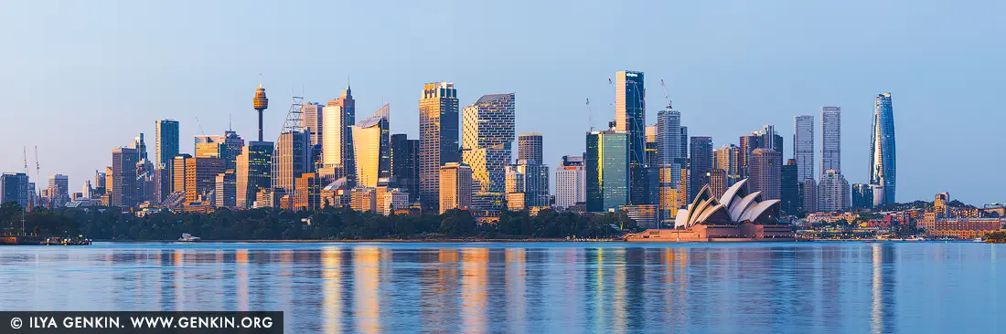 Luminous Dawn Over Sydney Harbour - Fine art print of Sydney, New South Wales (NSW), Australia - In the quiet moments just before sunrise, Sydney reveals a rare and poetic side of its character. From Cremorne Point, the city skyline stretches across the water in perfect balance, wrapped in the cool calm of blue hour while the first light of day ignites the eastern sky. Soft yellows and warm amber tones spill across the glass towers, setting them aglow, while the Sydney Opera House emerges as a radiant focal point - its sails kissed by early sunlight, glowing against the tranquil harbour. The water below mirrors this fleeting harmony of color and form, smoothing the city into painterly reflections that feel both expansive and intimate. There is a sense of anticipation in the air, a pause between night and day, where the city seems to breathe before waking. This panoramic artwork captures that delicate transition, blending serenity with quiet energy and timeless architectural beauty. Ideal for a living room, office, or refined commercial space, this piece brings light, optimism, and a sense of openness into any interior. It invites the viewer to linger, to feel the calm of early morning, and to experience Sydney not as a bustling metropolis, but as a luminous harbour city suspended in a moment of golden promise. - Image ID: AU-SYDNEY-0041