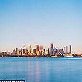 Golden Morning Calm Over Sydney Harbour - Fine art print of Sydney, New South Wales (NSW), Australia - Soft morning light settles gently over Sydney just after sunrise, revealing the city in a moment of perfect balance and quiet elegance. From Cremorne Point, the skyline rises confidently above the harbour, bathed in warm golden tones that contrast beautifully with the cool, silky blue of the water below. The Sydney Opera House glows in the early sun, its iconic sails catching the light like sculpted porcelain, anchoring the composition with timeless grace. This is a portrait of Sydney at its most serene - when the city has awakened, yet the day has not fully begun. Glass towers reflect the first warmth of sunlight, while the harbour smooths into long, tranquil reflections, creating a sense of space and clarity. The expansive sky adds breathing room to the scene, amplifying the feeling of openness and calm that defines this fleeting hour. There is an understated optimism in this image, a sense of promise carried by the morning light. It invites the viewer to slow down, to appreciate the harmony between architecture, water, and sky, and to experience the city not through movement, but through stillness. The square format enhances this balance, making the composition feel grounded, refined, and effortlessly modern. Perfect for contemporary living rooms, offices, or minimalist interiors, this artwork brings warmth, light, and quiet confidence into any space. It serves as a daily reminder of calm beginnings, fresh perspective, and the enduring beauty of one of the world's most iconic harbour cities. - Image ID: AU-SYDNEY-0042