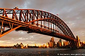 australia stock photography | Sydney Harbour Bridge and Opera House at Sunset, Sydney, New South Wales (NSW), Australia, Image ID AU-SYDNEY-HARBOUR-BRIDGE-0001. A beautiful picture of The Harbour Bridge and The Sydney Opera House at sunset. They are the two most famous Sydney and Australian icons and are well known all over the world. And the wharf near the Luna Park in Milsons Point is one of the best places to photograph the Harbour Bridge. Dark grey paint on the harbour bridge turned vermillion red due to very low sun.