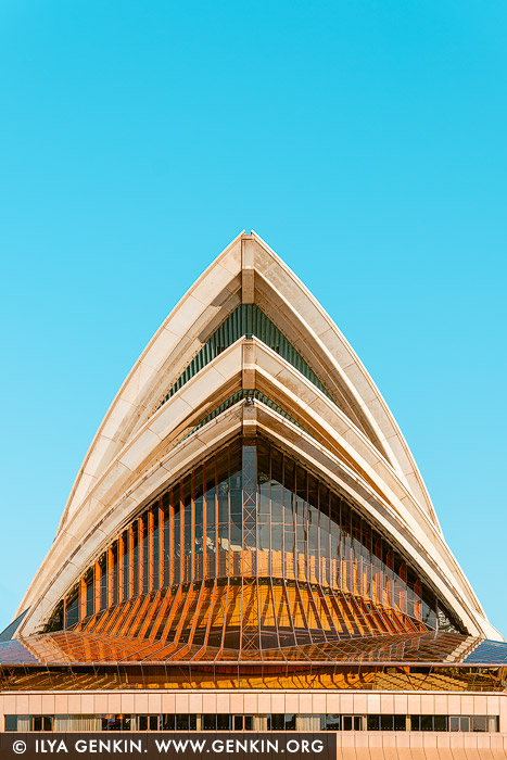 australia stock photography | Symphony of Light: Sydney Opera House in Stillness, Sydney, New South Wales (NSW), Australia. In this minimalist portrait of the Sydney Opera House, the iconic sails rise with sculptural elegance against a flawless blue sky, their geometry mirrored in tranquil harbour reflections below. Captured from a perfect frontal perspective, the image emphasises the harmony between form, light, and architectural rhythm. Warm golden hues glint through the layered glass and steel, hinting at the dynamic energy within, while the composition remains serenely still - almost meditative in its symmetry. This fine art print evokes both strength and grace, making it an ideal statement piece for modern interiors, creative studios, or serene office spaces seeking balance and inspiration.