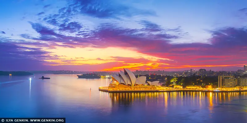 australia stock photography | Sydney Opera House at Sunrise, Sydney, New South Wales (NSW), Australia. The city is caught between night and day. A vivid band of color lifts over the harbour as the first light reaches the sails of the Opera House, turning the water into a smooth, reflective calm. The air feels still, almost hushed, as Sydney wakes beneath a sky alive with layered blues, purples, and fire-warm gold. This moment carries a sense of balance - energy without noise, drama without urgency. It speaks to beginnings and quiet confidence, where architecture and nature meet in perfect timing. The familiar landmark feels newly revealed, less iconic and more intimate, as if seen before the rest of the world arrives. On a wall, this image becomes a steady presence. It draws the eye without demanding attention, adding depth and light to living spaces, offices, or studios. The wide panoramic view opens a room, offering a daily reminder of clarity, scale, and calm momentum. This photograph is offered as a finely crafted wall art print, made to be experienced physically rather than glanced at in passing. The detail, color, and stillness are designed to hold their place in a room over time. Created to live on your wall, not just on a screen.