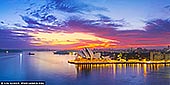 Sydney Opera House at Sunrise - Fine art print of Sydney, New South Wales (NSW), Australia - The city is caught between night and day. A vivid band of color lifts over the harbour as the first light reaches the sails of the Opera House, turning the water into a smooth, reflective calm. The air feels still, almost hushed, as Sydney wakes beneath a sky alive with layered blues, purples, and fire-warm gold. This moment carries a sense of balance - energy without noise, drama without urgency. It speaks to beginnings and quiet confidence, where architecture and nature meet in perfect timing. The familiar landmark feels newly revealed, less iconic and more intimate, as if seen before the rest of the world arrives. On a wall, this image becomes a steady presence. It draws the eye without demanding attention, adding depth and light to living spaces, offices, or studios. The wide panoramic view opens a room, offering a daily reminder of clarity, scale, and calm momentum. This photograph is offered as a finely crafted wall art print, made to be experienced physically rather than glanced at in passing. The detail, color, and stillness are designed to hold their place in a room over time. Created to live on your wall, not just on a screen. - Image ID: AU-SYDNEY-OPERA-HOUSE-0052