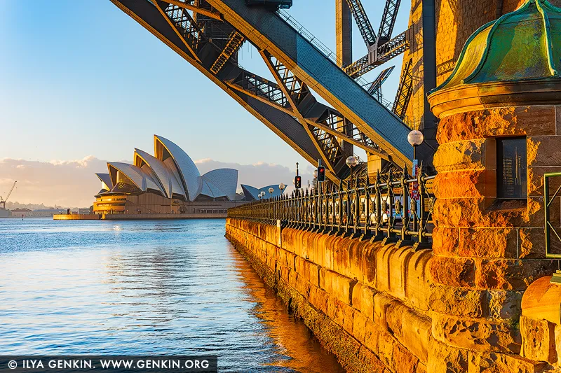 australia stock photography | Harbour Embrace, Sydney Opera House, Sydney, NSW, Australia. Bathed in the first gold of morning, this harbour scene brings a sense of calm momentum into a space. The glowing stone, quiet water, and luminous sails create an atmosphere of poised stillness, where the city feels softened into ritual and light becomes a symbol of renewal. Living alongside it invites a slower breath, a clearer mind, and a feeling of openness that lingers throughout the day. As a commanding visual focal point, this piece anchors refined living rooms, entrance halls, and executive interiors with both structure and serenity. Its warm amber tones and cool harbour blues shift beautifully with natural light across the wall, offering depth from dawn through evening. In a commanding, large-format museum presentation, the architectural lines and radiant colour truly come alive, expanding the perceived boundaries of the room and giving the space a more elevated, considered presence.