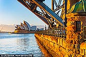 Harbour Embrace, Sydney Opera House - Fine art print of Sydney, NSW, Australia - Bathed in the first gold of morning, this harbour scene brings a sense of calm momentum into a space. The glowing stone, quiet water, and luminous sails create an atmosphere of poised stillness, where the city feels softened into ritual and light becomes a symbol of renewal. Living alongside it invites a slower breath, a clearer mind, and a feeling of openness that lingers throughout the day. As a commanding visual focal point, this piece anchors refined living rooms, entrance halls, and executive interiors with both structure and serenity. Its warm amber tones and cool harbour blues shift beautifully with natural light across the wall, offering depth from dawn through evening. In a commanding, large-format museum presentation, the architectural lines and radiant colour truly come alive, expanding the perceived boundaries of the room and giving the space a more elevated, considered presence. - Image ID: AU-SYDNEY-OPERA-HOUSE-0054