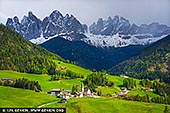  stock photography | Storm Approaching Santa Maddalena, Santa Maddalena, Dolomites, Bolzano - South Tyrol, Italy, Image ID ITALY-DOLOMITES-0002. In this late spring scene, the village of Santa Maddalena nestles peacefully in the heart of the Dolomites, bathed in the soft, diffused light of a late afternoon. The rolling fields below glow in lush, almost surreal shades of green - alive with new growth and warmth - while the towering peaks above remain streaked with snow, reminders of a winter not long gone. Looming on the horison, heavy storm clouds begin to drift in, casting long shadows across the valley and adding a dramatic tension to the landscape. The iconic church of Santa Maddalena, with its slender steeple and quiet presence, anchors the scene - a symbol of calm and resilience as nature prepares to shift once again.