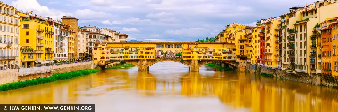 Timeless Charm of Ponte Vecchio in Soft Light - Fine art print of Florence, Tuscany, Italy - Under a canopy of soft, cloud-strewn skies, the Ponte Vecchio stretches gracefully across the golden-tinted Arno River, glowing with centuries of Florentine history. The rich yellows and warm ochres of the historic buildings lining the bridge and riverbanks seem to hum with quiet elegance. In this panoramic composition, the timeless architecture draws the eye toward the heart of Renaissance Florence - a place where artisans once traded gold and dreams. The gentle light, mirrored in the calm waters below, evokes a feeling of warmth and nostalgia. This artwork brings a refined, European touch to any interior - ideal for adding character and cultured beauty to a living space or office. - Image ID: ITALY-FLORENCE-0003