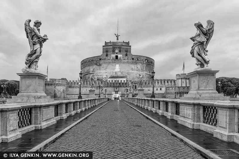 italy stock photography | Echoes of Eternity: Ponte Sant'Angelo in Monochrome, Rome, Lazio, Italy. Captured in striking black and white, this view down the Ponte Sant'Angelo toward Castel Sant'Angelo evokes a timeless reverence. The angels that line the bridge stand as silent sentinels, their sculpted wings poised above the cobblestones worn by centuries of footsteps. The absence of color intensifies the drama - every shadow, every stone, every crack in the ancient architecture tells a story of empire, devotion, and endurance. Under a moody Roman sky, this image becomes more than a photograph; it is a portal into the soul of the Eternal City. A compelling centrepiece for minimalist or monochrome-themed interiors, perfect for spaces seeking quiet strength and historical depth.