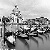  stock photography | Basilica Santa Maria della Salute, Venice, Veneto, Italy, Image ID ITALY-VENICE-0005. In this black and white long exposure, Venice transforms into a dreamscape. The Basilica di Santa Maria della Salute rises in quiet majesty, its Baroque silhouette softened by the misty blur of time. In the foreground, classic gondolas float like ghostly silhouettes, gently tethered yet drifting in the liquid stillness. The water, smoothed into glass by the long exposure, erases all trace of motion - a mirror of memory rather than a record of reality. Above, a pale, cloud-veiled sky dissolves into light, creating a minimalist backdrop that draws every eye to the domes and curves of the basilica. This image captures not just a scene, but a feeling: the stillness between tides, the silence between centuries.