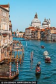  stock photography | The Grand Canal at Ponte dell'Accademia #2, Venice, Veneto, Italy, Image ID ITALY-VENICE-0008. Late afternoon light bathes Venice in a golden glow as the Grand Canal unfurls beneath the wooden arch of Ponte dell'Accademia. From this vantage point, the Baroque dome of Santa Maria della Salute rises like a sentinel of resilience - built in the 17th century as a votive offering after a devastating plague claimed nearly a third of the city's population. Designed by Baldassare Longhena, its octagonal silhouette and luminous Istrian stone facade have become synonymous with Venetian grace. Below, the canal pulses with life: gondolas glide past vaporettos, their wakes weaving patterns of light across the water. Palazzos line the banks, their weathered facades reflecting centuries of history.