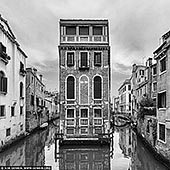  stock photography | Venice Canals and Streets, Study 1, Venice, Veneto, Italy, Image ID ITALY-VENICE-0009. In this striking black-and-white capture, a narrow Venetian palazzo rises like a surreal stage set, perfectly framed between two quiet canals. The stark symmetry and elegant arches of the building's facade contrast beautifully with the soft ripples below, while the surrounding alleyways curve gently out of view, hinting at the labyrinthine charm of Venice. Stripped of color, the scene feels timeless - its textures and geometry more pronounced, the silence almost audible. This image encapsulates the poetic stillness of Venice, where history, architecture, and water intertwine in a dreamlike balance.