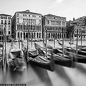  stock photography | Venice Grand Canal, Study 3, Venice, Veneto, Italy, Image ID ITALY-VENICE-0010. Elegance drifts across time in this black-and-white long exposure of Venice's Grand Canal. Moored gondolas sway gently in blurred motion, their iconic silhouettes ghostlike against the still water, evoking the city's ceaseless rhythm. Behind them, the regal facades of historic palazzi - lined with columns, arches, and timeworn textures - stand in quiet contrast, frozen in architectural splendor. This poetic image captures the tension between movement and stillness, between the living flow of the canal and the enduring presence of Venetian grandeur. A timeless portrait of a city where water and stone dance in harmony.