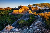 landscapes stock photography | Pagoda Lookout at Sunrise, Dunns Swamp, Wollemi National Park, New South Wales (NSW), Australia, Image ID AU-PAGODA-WOLLEMI-0001. The spectacular pagoda rock formations at Dunns Swamp are Triassic age Narrabeen Sandstone formed by the deposition of water borne sediments, approximately 200 million years ago. The type of sediment deposited is determined by the flow of the water, with gravel, forming conglomerate, deposited by fast running water; sand, forming sandstone, deposited by slower running water, and silt, forming shale, deposited by slow running water. At Dunns Swamp, there is a very thick layer of sandstone with no intervening layers of shale. As a result of earth movements, vertical cracks called joint planes form in the sandstone and cause it to break along these joints into roughly rectangular blocks. Water running across the joint planes erodes the rock more quickly than in the centre of the sandstone blocks, and the top of each block becomes a dome shape. Where two joint planes meet, weathering on the edges is more aggressive and the rectangular blocks tend to become oval in shape. Differential weathering patterns are created when differences in texture of the sandstone causes some layers to wear more quickly than others, generating the terraced appearance of the domes.