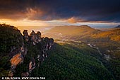 landscapes stock photography | The Three Sisters at Dramatic Sunrise, Echo Point, Katoomba, Blue Mountains, NSW, Australia, Image ID THREE-SISTERS-BLUE-MOUNTAINS-0006. The Three Sisters are an icon of the Blue Mountains and NSW. These three pillars can be seen from the viewing platform at Echo Point in Katoomba, Blue Mountains, NSW, Australia. There is a fascinating Aboriginal dream-time legend that explains the story of the sisters and how they got there: The story tells of three sisters who were part of the Katoomba tribe who lived in the Jamison Valley. The three young women, Meehni, Wimblah and Gunnedoo had fallen in love with three boys (who were also brothers) from the Nepean tribe. However they weren't able to marry because of tribal law. The brothers upset by this decided to capture the three sisters, which started a battle between the two tribes. A witchdoctor from the Katoomba tribe took it upon himself to protect the sisters from harm, but turning them into stone for protection. He was killed during the battle so he was unable to turn them back to flesh like he planned to, after the battle was over. The sisters are still beautiful in their rock formation and remain there as a reminder of the battle that took place between the two tribes.