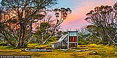 landscapes stock photography | Wallace's Hut at Sunset, Falls Creek, Victoria, Australia, Image ID AU-FALLS-CREEK-WALLACES-HUT-0004. Wallace's hut was built in 1889 and is probably the oldest surviving hut on the high plains of north-east Victoria. It was built in six weeks by Irish immigrant brothers Arthur, William and Stewart Wallace among old snow gums on a grassy plain above the snowline. The brothers held grazing leases on the High Plains and the hut was built to provide shelter for the cattlemen working there. The timber was cut from the forest about four hundred metres east of the hut, and the hearth stone was dragged in from Pretty Valley. The chimney had a base of rubble and above this iron sheeting on a timber frame. The slab walls were lined with hessian and later with tar-paper, and inside there was a bush table, sleeping platform and a rustic fire-side settle. The hut was used by many local cattlemen, as well as stockmen from New South Wales, who brought sheep here during the 1914-18 drought. Many such huts were built in mountain areas, but they were flimsy structures, and at great risk from bush fires, and no others have survived from the nineteenth century. The State Electricity Commission used the hut from the late 1920s until the early 1940s to collect data on precipitation for possible future hydroelectric works, and SEC employee Joe Holsten covered the roof and later the walls with corrugated iron, renewed the chimney and added a skillion for storing firewood and horse feed. In the 1940s the Rover section of the BoyScout Association took over responsibility for maintenance and it became an important refuge and destination for walkers and skiers.