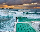 landscapes stock photography | Waves Crushing at Bondi Icebergs, Bondi Beach, Sydney, NSW, Australia, Image ID AU-BONDI-BEACH-0006. Huge waves crashing over the swimming pools at the Bondi Icebergs Club on a beautiful morning in Sydney, NSW, Australia. Sydney's most famous beach is Bondi. At its southern end is Bondi Baths or Bondi Icebergs swimming pool, an eight-lane, 50-meter saltwater pool built into the cliffs. Open every day except Thursdays, it is home to the Bondi Icebergs Club, which was founded in 1929 by a small group of friends. To become an Icebergs member you must swim three of every four Sundays for five years during the winter (May to September Down Under). It is a true test of dedication, for while outsiders might think that Australia is the land of endless summer, in winter the ocean water is teeth-chattering cold. And on opening day of the winter swimming season, it is tradition that lumps of ice are tossed into the pool to test the hardiness of the competitors.