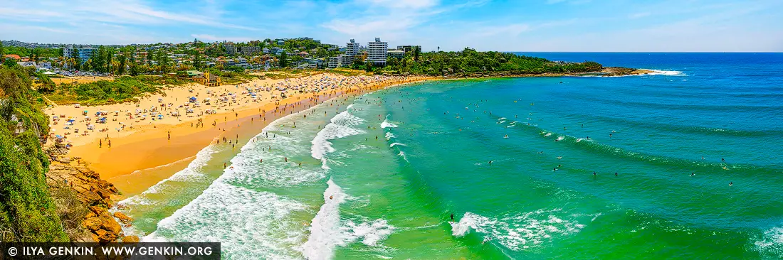 Emerald Break at Freshwater Beach - Fine art print of Sydney, NSW, Australia - The vibrant emerald waters of Freshwater Beach shimmer beneath the Australian summer sun, drawing surfers by the dozens to its rolling waves. From this elevated perspective, the golden arc of sand is alive with beachgoers, umbrellas, and laughter, set against a backdrop of leafy headlands and coastal homes. The swell glides in with rhythmic grace, catching the light and surfers alike, as the energy of the day hums across land and sea. A perfect harmony of movement, color, and life, this panoramic coastal artwork infuses any room with warmth and vitality - an uplifting centrepiece for beach houses, bright living spaces, or creative retreats. - Image ID: AU-FRESHWATER-BEACH-0006