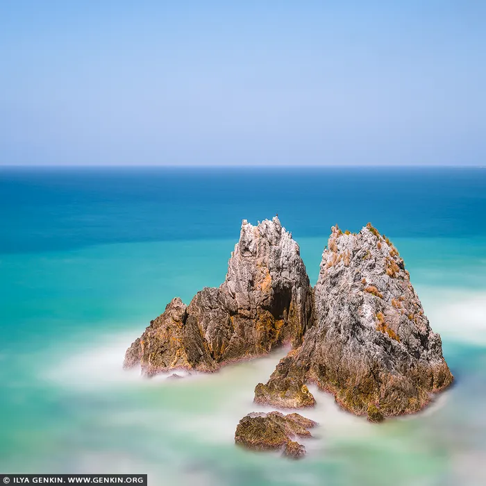 landscapes stock photography | Quiet Strength, Camel Rock, Bermagui, Sapphire Coast, NSW, Australia. Rising from soft turquoise water, weathered stone holds its ground beneath an open blue sky. Pale ribbons of surf soften the jagged contours, while warm ochre traces bring depth to the rock. There is a quiet balance here between strength and surrender - a steady presence surrounded by space, inviting the mind to slow down. As a visual anchor in a refined residential or executive space, the sculptural formation gives the eye somewhere to rest. Its blues and sea greens lend an airy quality to the wall, balanced by earthy gold and grey. Presented at a commanding scale with museum-quality finishing, the fine textures come forward, and the open horizon extends the room's sense of space.