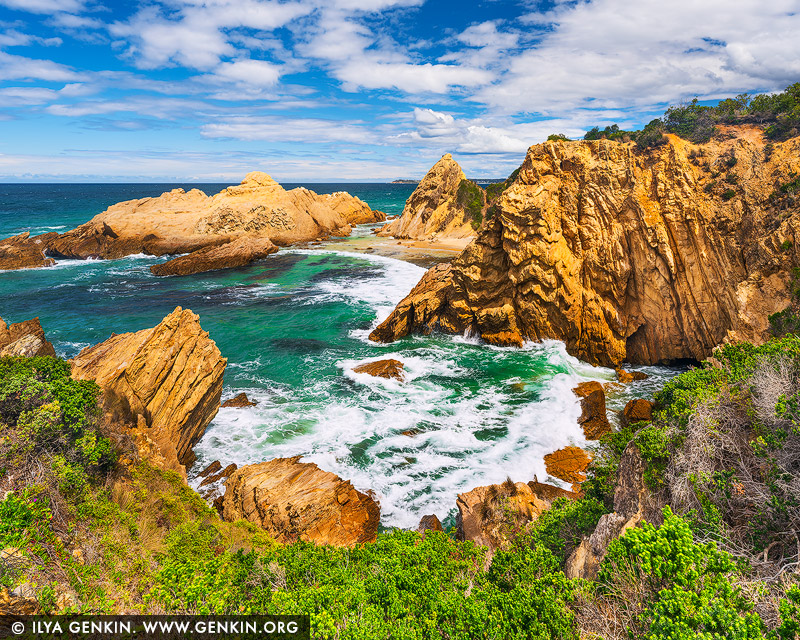 landscapes stock photography | Gilded Rhythm, Murunna Point near Bermagui, Sapphire Coast, NSW, Australia. Sunlit golden rock rises above turquoise water, while white surf traces a restless rhythm through the sheltered inlet. At Murunna Point, the meeting of solid stone and flowing sea brings both energy and reassurance: a sense of enduring strength beneath an open, cloud-strewn sky. Living alongside this scene offers a daily invitation to breathe more freely and reconnect with the coast. As a commanding focal point in a refined living room or executive space, warm ochre cliffs balance the cooler depths of blue and green. Their luminous tones lend warmth to a light-filled wall, while the intricate rock formations reward closer attention. In a large-format museum presentation, the inlet gains an enveloping presence, drawing the eye towards the horizon and extending the room's sense of space.