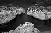 landscapes stock photography | Loch Ard Gorge in Black and White, The Twelve Apostles, Great Ocean Road, Port Campbell National Park, Victoria, Australia, Image ID APOST-0036. The Loch Ard Gorge is part of Port Campbell National Park, Victoria, Australia, about three minutes' drive west of The Twelve Apostles. The gorge is named after the clipper ship Loch Ard, which ran aground on nearby Muttonbird Island on 1 June 1878 approaching the end of a three-month journey from England to Melbourne. Of the fifty-four passengers and crew, only two survived: Tom Pearce, at 19 years of age, a ship's apprentice, and Eva Carmichael, an Irishwoman emigrating with her family, at 19 years of age. According to memorials at the site, Pearce was washed ashore, and rescued Carmichael from the water after hearing her cries for help. Pearce then proceeded to climb out of the gorge to raise the alarm to local pastoralists who immediately set into plan a rescue attempt. After three months in Australia Carmichael returned to Europe. Four of her family members drowned that night. Pearce was hailed as a hero, and continued his life living until age 49. He is buried in Southampton, England.