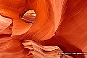 landscapes stock photography | Eye Of The Antelope, Lower Antelope Canyon, Navajo Tribal Park, Page, Arizona, USA, Image ID US-ARIZONA-ANTELOPE-CANYON-0002. Cascading shapes and curves of red sandstone reflected by natural light reflect a beautiful scenic landscape unique to the Antelope slot canyons of the Colorado Plateau in Navajo Land near Page, Arizona. Carved through iron rich Navajo Sandstone, Antelope Canyon is one the many slot canyons of the Colorado Plateau sculpted by flash floods during the monsoon season of late summer. Though these slot canyons are carved into many different geological layers of sandstone and limestone, it is the Navajo Sandstone, formed from the petrified sand dunes of a large Jurassic desert similar to the Sahara Desert of today, that often become the richest canvas for the flash floods to carve their masterpieces through. These canyons become otherworldly sculptures of stone that slowly evolve over time.