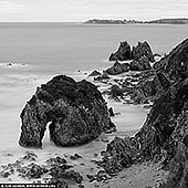 Silent Sentinel - Horse Head Rock - Fine art print of Bermagui, Sapphire Coast, NSW, Australia - Dark, weathered stone rises from a silver sea, its sculpted arch offering a quiet passage through the rock. Soft water surrounds the rugged formations, setting their enduring strength against an almost weightless stillness. There is a grounding presence here: a sense of time slowing, space opening, and the everyday settling into perspective. As a commanding focal point in a refined living room or executive space, the interplay of charcoal, silver and pale grey brings depth without relying on colour. Lighter passages respond to daylight, while richly textured shadows hold the composition firmly on the wall. Presented at a generous scale in a museum-quality finish, the intricate coastline and open horizon draw the eye beyond the room's boundaries. - Image ID: AUSTRALIAN-COAST-BW-0011