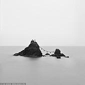 portfolio stock photography | Meoto Iwa #3 (The Wedded Rocks), Futami, Mie Prefecture, Japan, Image ID JAPAN-MEOTO-IWA-0003. The two rocks, known as Izanagi and Izanami respectively, are together called Meoto Iwa and are connected at all times by a thick rope that tethers the lovers together. The stones are seen as a representation of paired dualities, hence the outcroppings have gained nicknames such as the 'lover's rocks' and the 'wedded rocks.' Physically, the stones are not remarkably large, with the larger of the two (Izanagi) standing just nine meters tall and the smaller one (Izanami) just over three meters. However, the key feature of the site is the shimenawa, a thick rope made of rice straw that has been braided in a specific way that is sacred to the Shinto religion. The huge rope wraps around both rocks and is said to weigh at least a ton. The cord is continually eroded by sea water and the elements, but it replaced three times a year in a special ceremony.