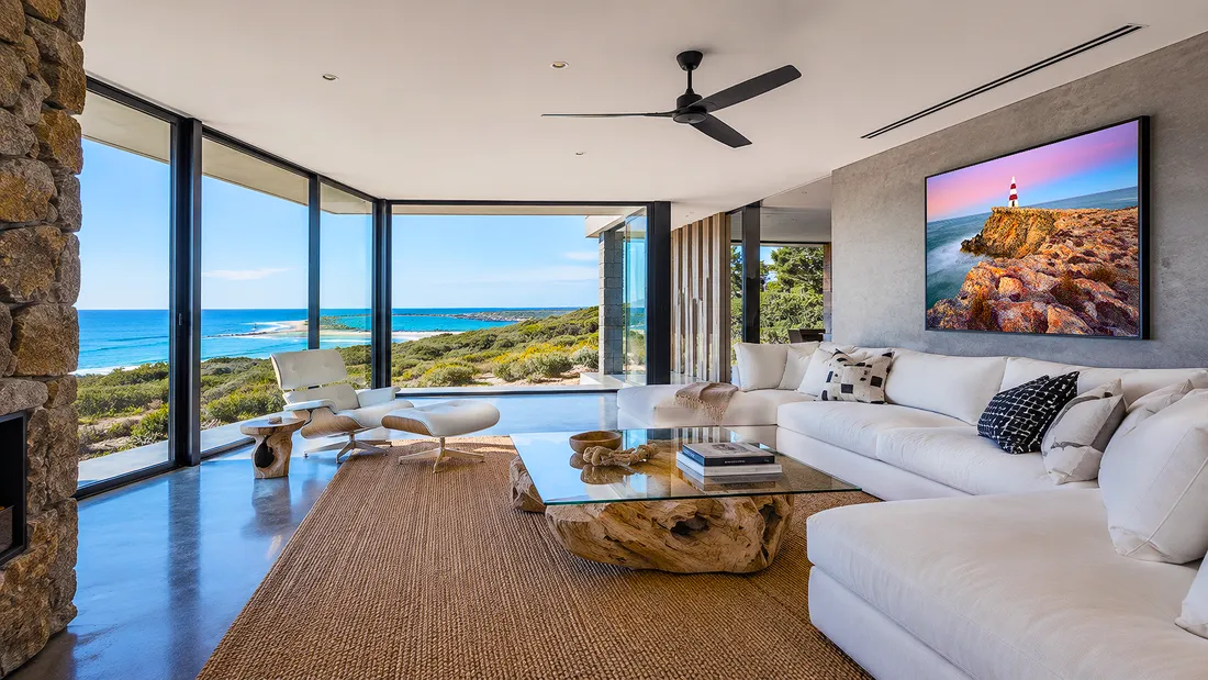 Luxury Australian coastal living room with ocean views, stone feature wall, white sofa and colourful lighthouse wall art above the couch
