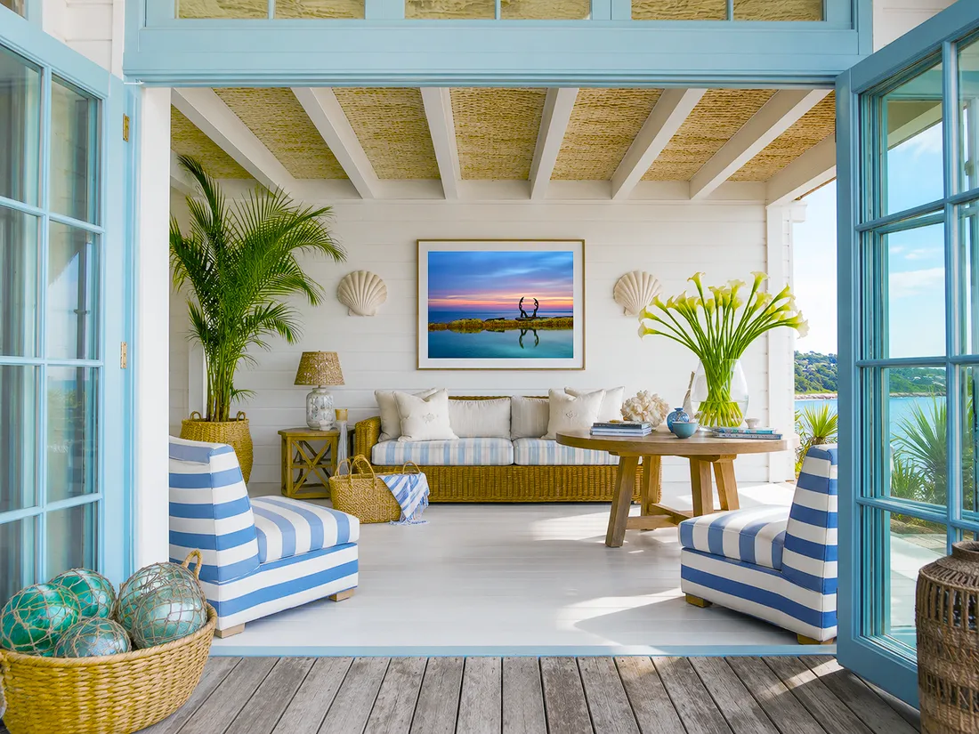 Australian coastal verandah with blue French doors, striped chairs, rattan furniture and colourful sunset wall art above the sofa