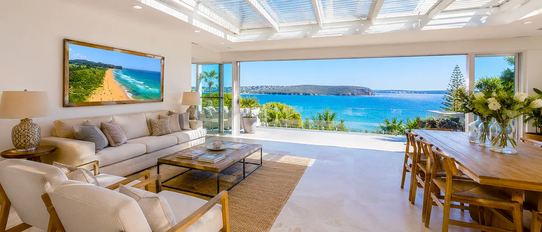 Bright Australian coastal living room with ocean views, neutral furniture and colourful beach wall art above the sofa