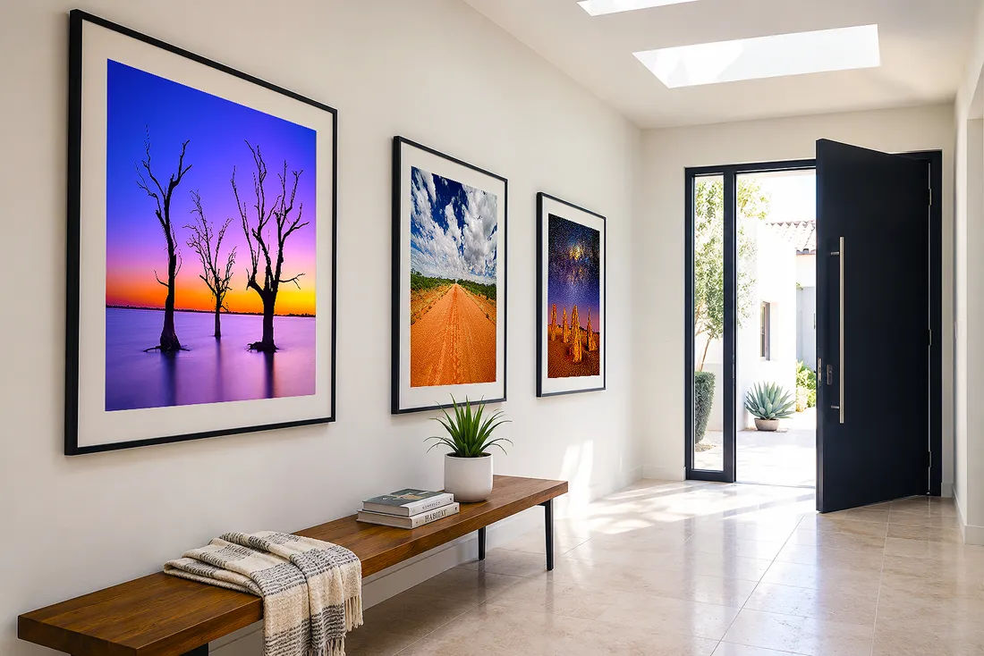 Bright modern entryway with three framed landscape photographs hung above a wooden bench near an open front door.