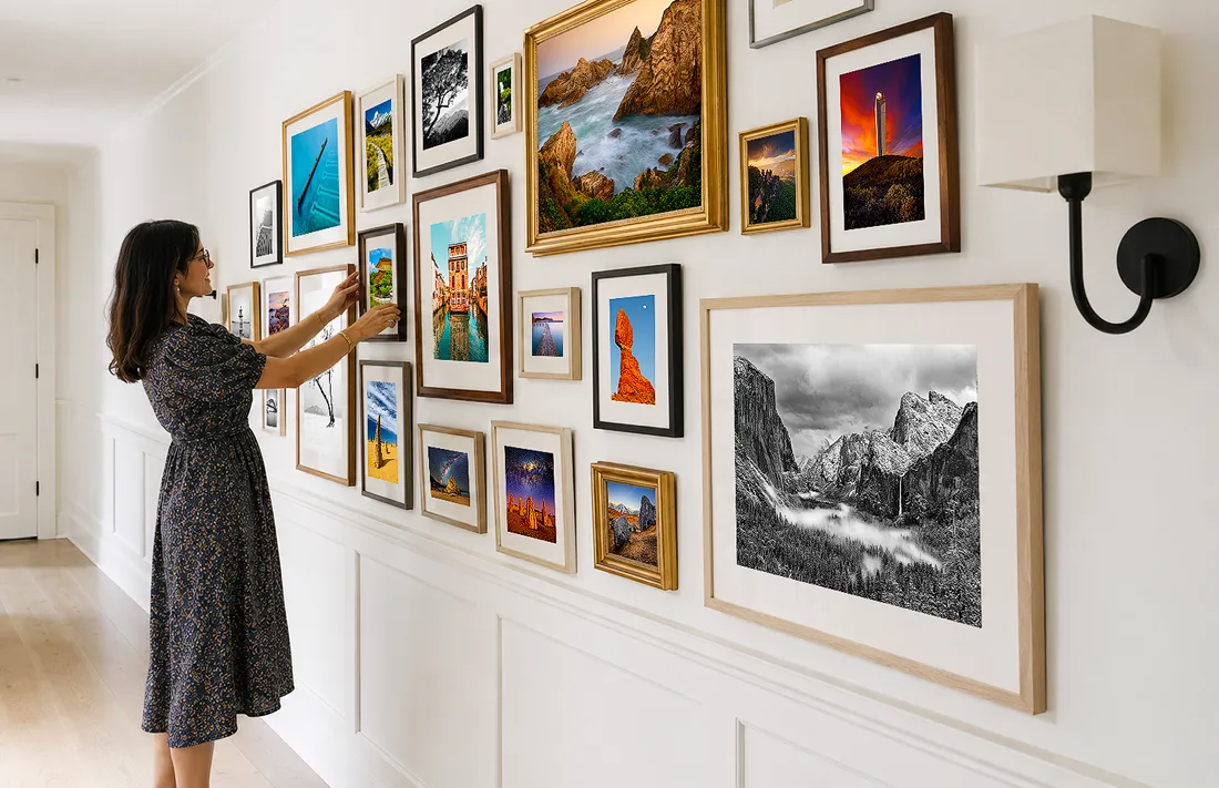 Hallway gallery wall with mixed framed landscape photographs and artworks, with a person adjusting one of the frames in a Luxury Home.