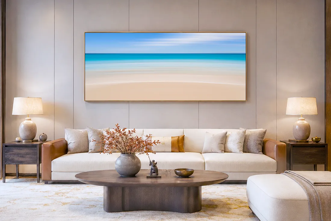 Living room with a large horizontal beach photograph hung above a long sofa, showing how wide artwork can balance the sofa below.