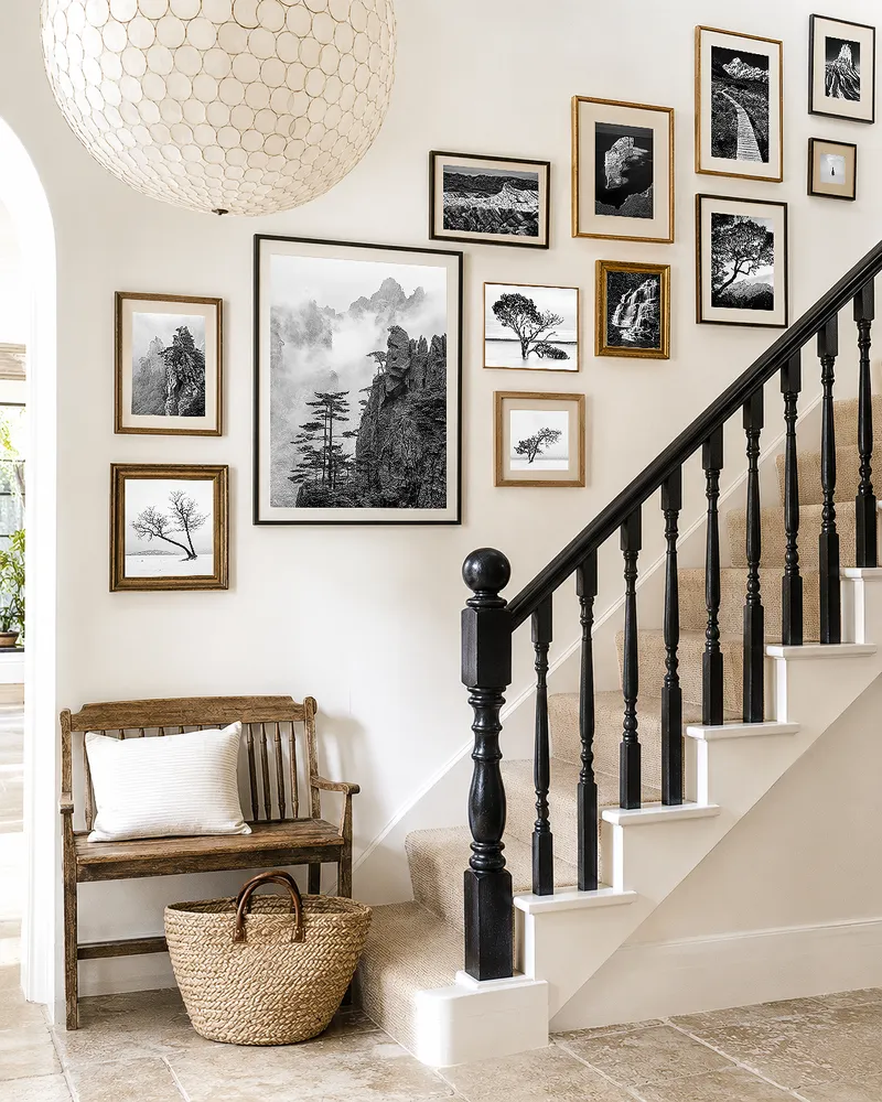 Staircase wall with a gallery arrangement of framed black and white landscape photographs following the rising line of the stairs in a luxury home.