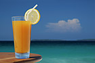 Glass of Juice with Lemon Twist and Straw Against Tropical Sea.