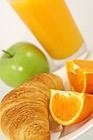 Fresh-baked croissant, green apple, orange juice and wedges. Shallow DOF. Focus on croissant.